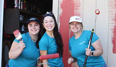 Volunteers with paint brushes in front of a barn